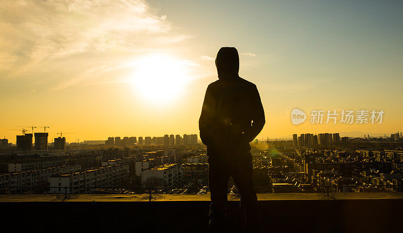 年轻人站在屋顶上，看着城市的夕阳