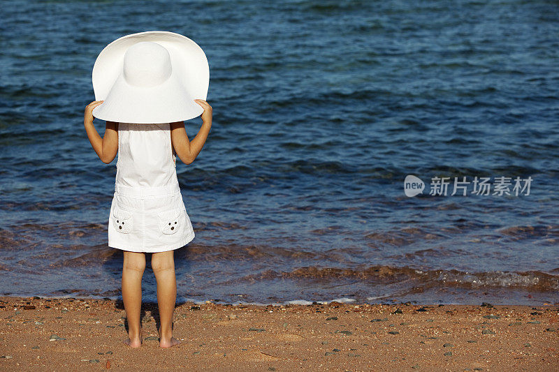 小女孩戴着白色太阳帽站在海滩上