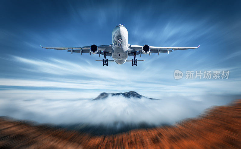 飞机的运动模糊效果是飞过低空云层。景观有客机，模糊的云，山，蓝天。乘飞机。商务旅行。商用飞机。概念