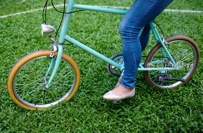 蓝色复古自行车站在绿色草地上，和穿着牛仔裤的女人在一起。