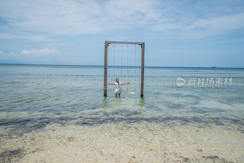 年轻女子双臂伸展在海上荡秋千，巴厘岛，印度尼西亚