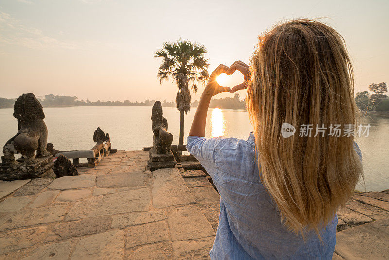 一个年轻女子在柬埔寨旅行，喜欢吴哥窟的庙宇，用手做一个心形的手指框架。