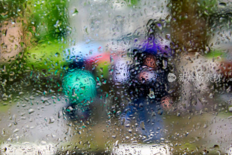 雨滴在玻璃上，人们拿着蓝色的伞