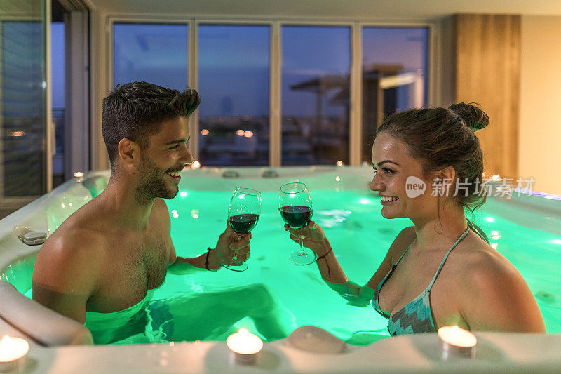 年轻幸福的夫妇享受红酒在热水浴缸。