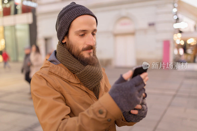 留胡子的年轻人在街上看智能手机