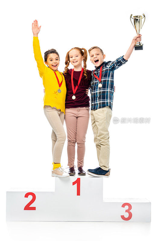 快乐的孩子们拿着奖章和奖杯站在胜利者的基座上，大喊大叫，看着摄像机孤立在白色上