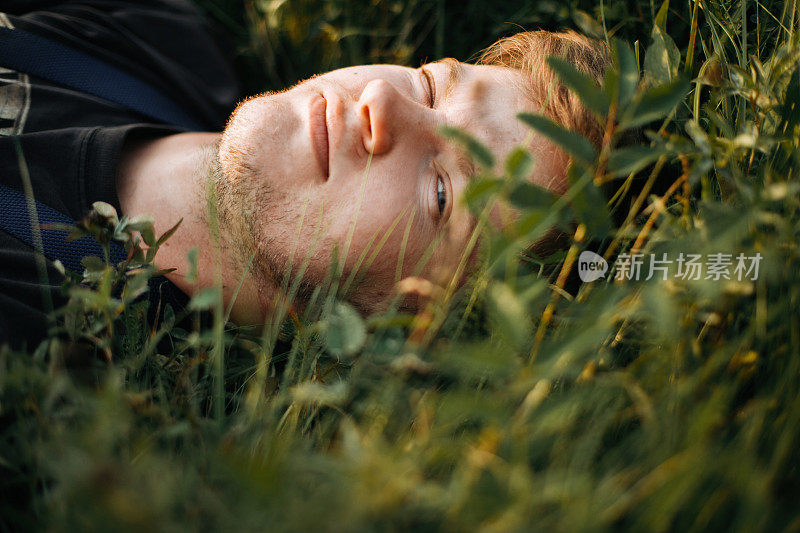 时尚潮男躺在绿色的草地上，在阳光明媚的草地上放松在大气的日落。帅哥在大自然中休息，在山中享受夜晚。空间的文本