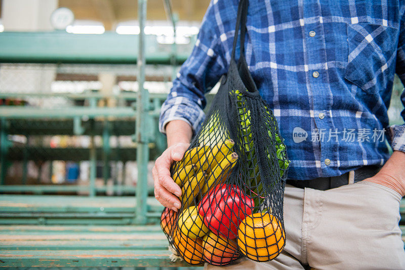 成年人与水果和蔬菜在一个黑色棉网可重复使用的袋子，零浪费购物在户外市场