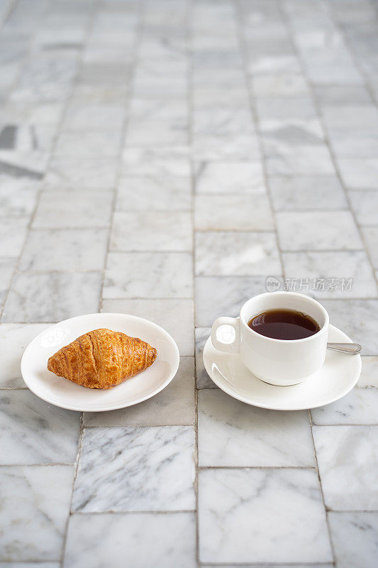 白杯子里装着牛角面包和黑咖啡，茶托放在大理石地板上