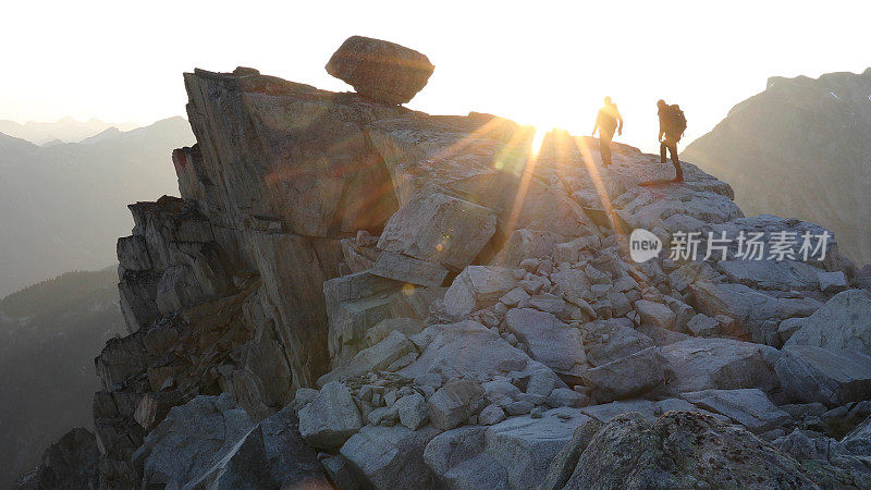 登山运动员在日出时沿着多岩石的峰顶徒步旅行