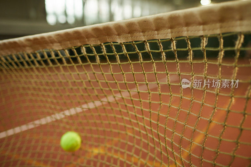 对网球击网失误的特写，聚焦于室内场地的网球网，复制空间