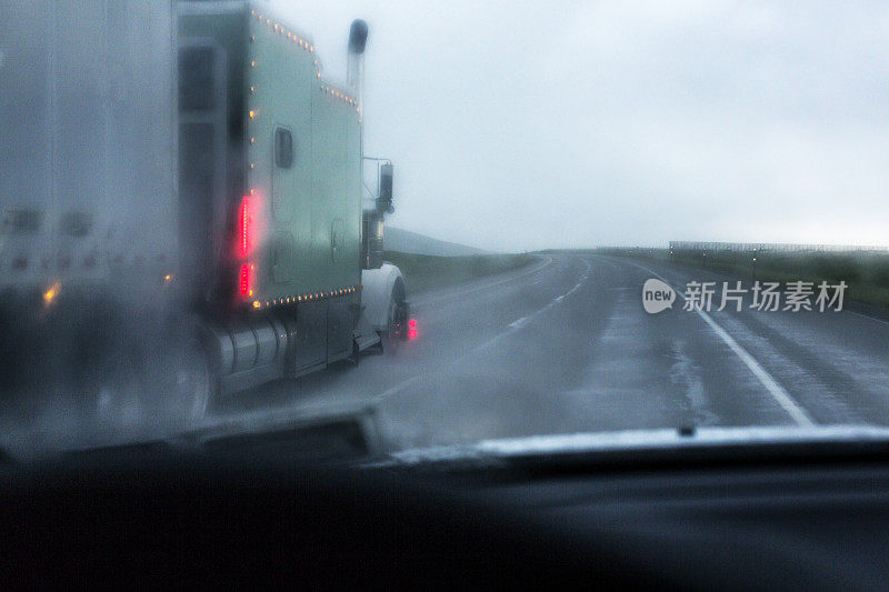 在被雨浸湿的高速公路上，半挂车与汽车擦肩而过