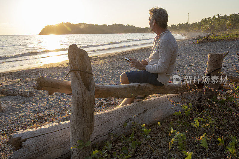 男子在热带海滩边放松，一边发短信