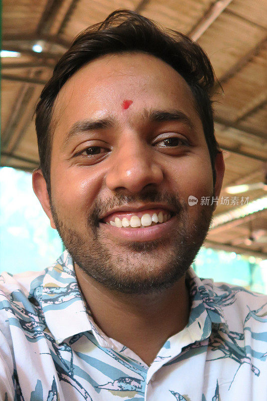 快乐的年轻印度印度教男子微笑与完美的白牙齿和红色的宾蒂滴点在前额，第三眼宾都戴的印度教徒和耆那教徒的颜色与猩红朱红粉，英俊的年轻男子在印度与短胡子茬丛林