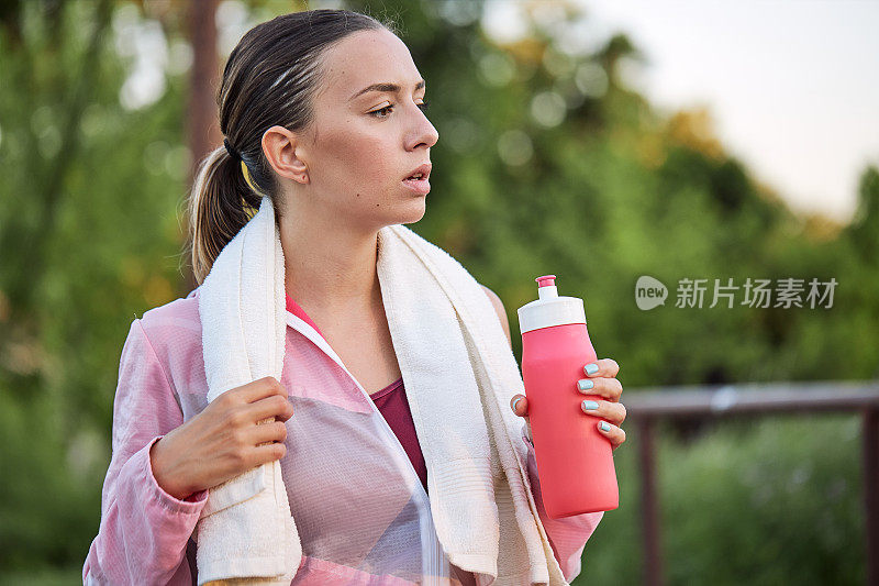 疲惫的年轻女运动员在跑步后拿着水瓶