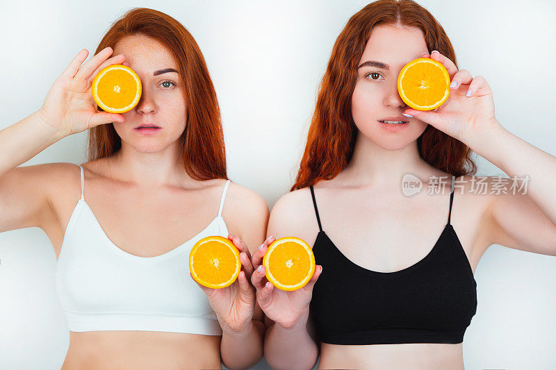两个红头发的年轻女子都看起来很有吸引力，站在孤立的白色背景手中拿着一半的橙子，美丽的肖像概念