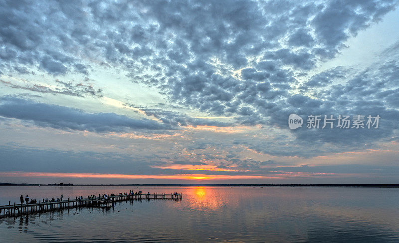 人们的剪影在码头湖边的黄昏与雄伟的云彩景观