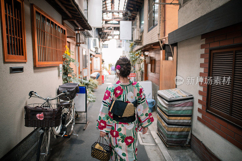 后视图的年轻女子在yukata走在狭窄的购物街
