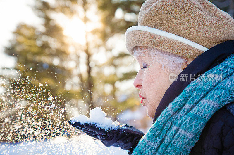 在一个阳光明媚的冬天下午，一位年长女性在她的手套上吹雪的侧面视图