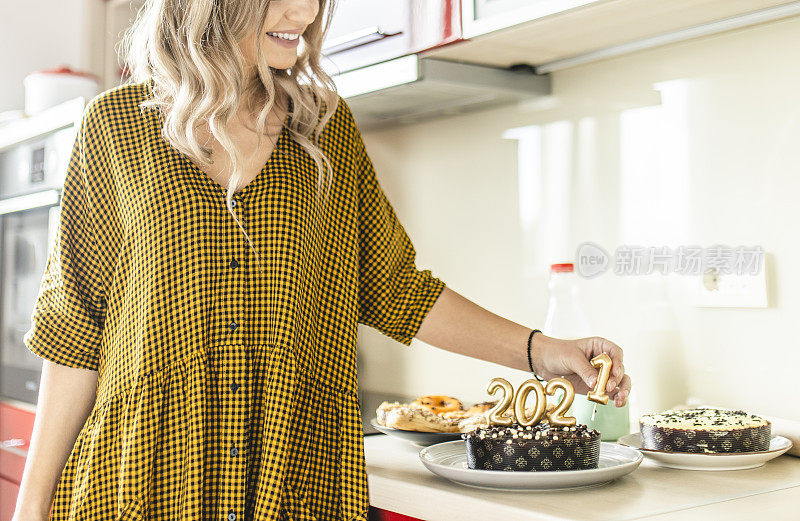 年轻女子制作和装饰巧克力蛋糕与点燃的蜡烛形状的数字2021新年派对的特写