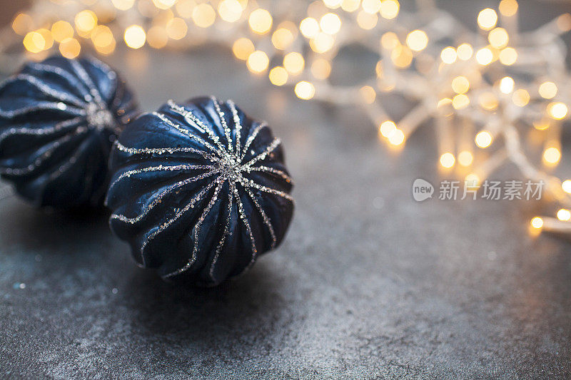 黑色的表面上点缀着蓝色的圣诞装饰物，带有模糊的串灯和复制空间