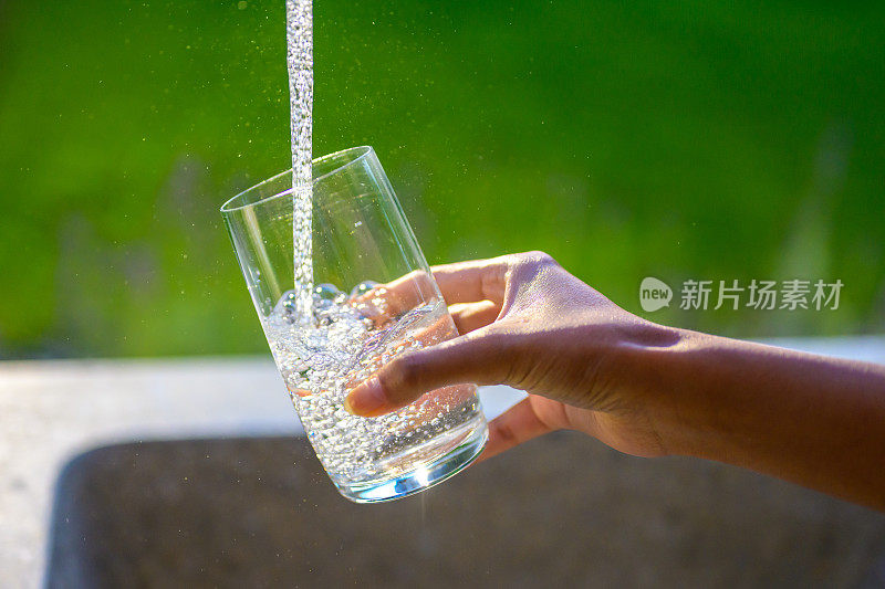 从水龙头里往玻璃杯里注入新鲜的水