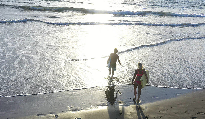 成熟的夫妇走在海滩上，带着冲浪板冲进水里