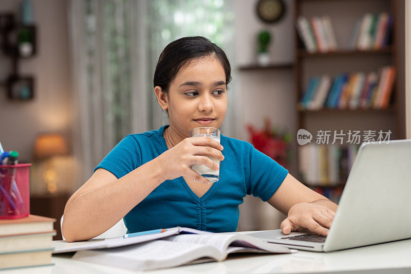 一个十几岁的女学生在家学习时喝牛奶的照片:库存照片