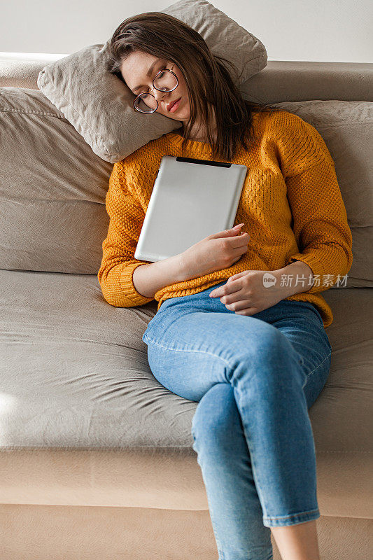 一名年轻女子用着平板电脑睡在沙发上