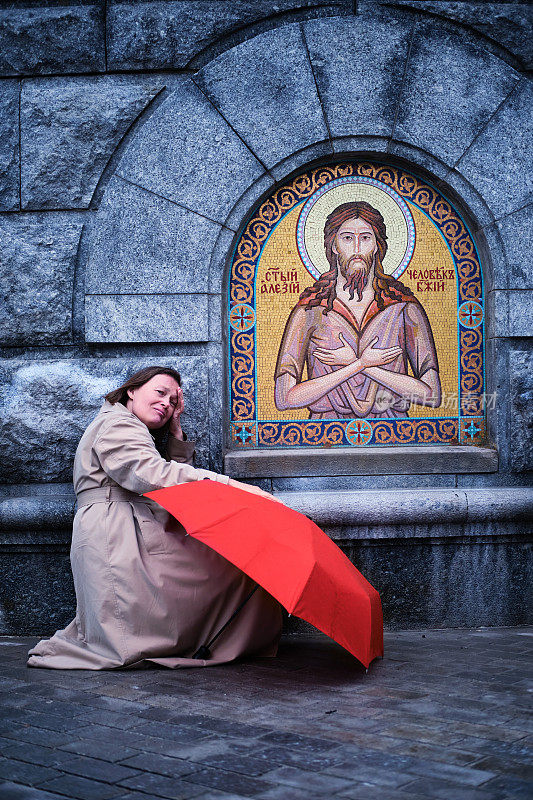 一个拿着伞哭泣的女人站在耶稣基督的圣像前