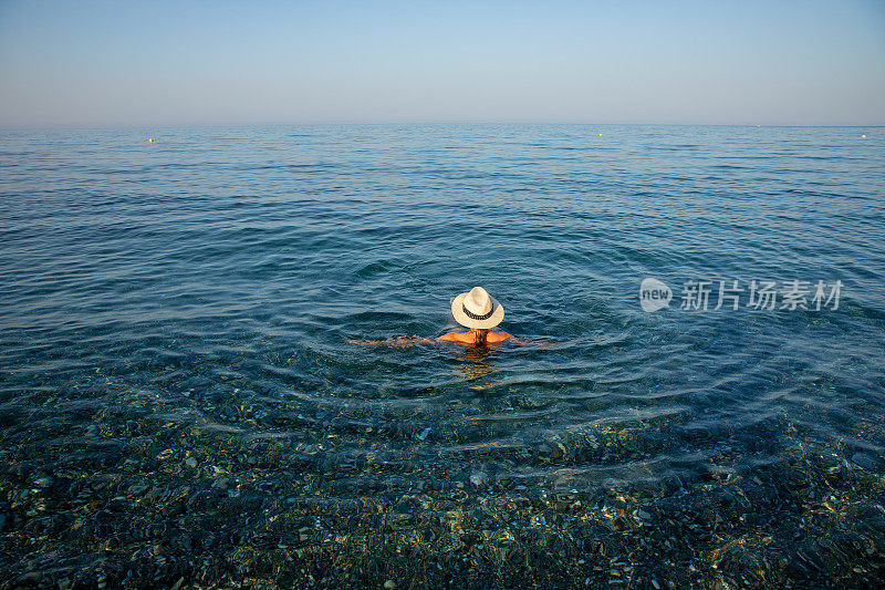 戴着太阳帽的年轻女子在海水里游泳