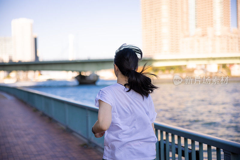 在城市的河边奔跑的女人的背面