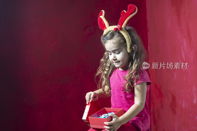 可爱的小女孩戴着圣诞驯鹿的鹿角，手里拿着礼盒