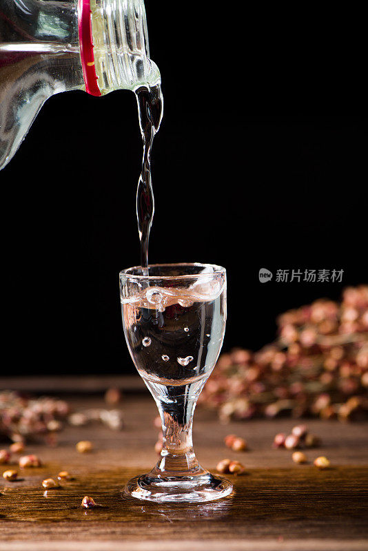 在木头背景上，中国白酒从瓶子里倒进玻璃杯里