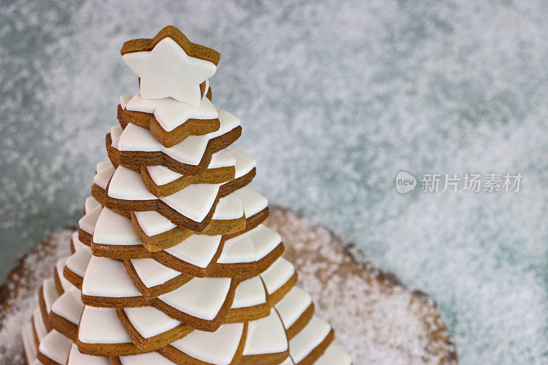 近距离拍摄的圣诞树是由堆在木蛋糕架上的姜饼星饼干上的白色皇家糖霜做成的，以人造雪为背景，高视野，聚焦于前景