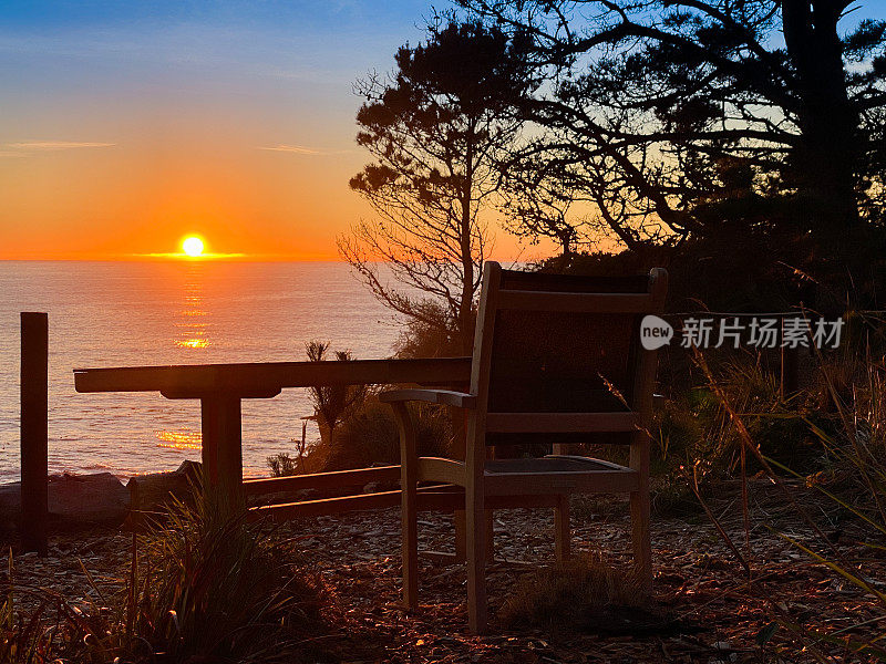 日落时分在太平洋边上的悬崖上的椅子和桌子