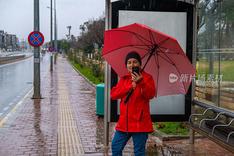 一位女士在雨天撑着伞在公共交通车站等车