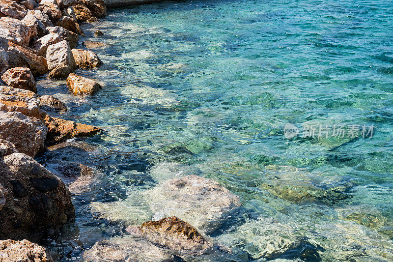 白色泡沫的海浪拍打着空旷的岩石海滩上粗糙的岩石。夏天阳光灿烂的日子