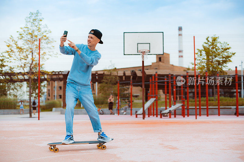 年轻的潮男滑板自拍与手机，而坐在滑板户外