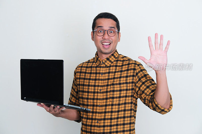 成年亚洲男子拿着笔记本电脑，伸出五指，露出快乐的表情