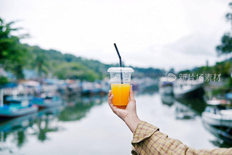 画像女人手拿塑料杯橙汁在早晨。