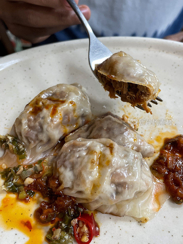 画面是一个陌生的人用金属叉子吃混合馄饨(中国的饺子)，里面有鸡肉、猪肉或鸭肉，洒上辣酱，重点放在前景上