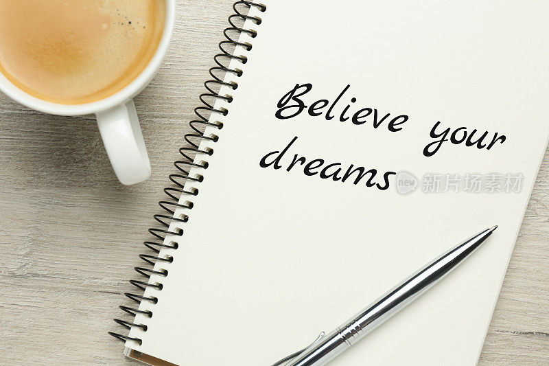 励志名言“相信你的梦想”写在笔记本上，放在木桌上，平铺