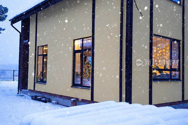 温馨的节日窗户的房子外面与仙女灯花环温暖的光-庆祝圣诞节和新年在一个温暖的家。圣诞树，散景，松树上的雪和雪