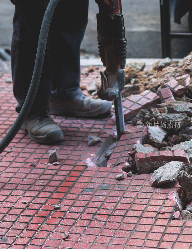 新人行道施工过程中，用手提钻修补人行道路面，施工工人用气锤和钻孔设备在施工现场破坏沥青路面和混凝土的过程