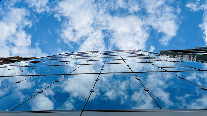 仰望高大的玻璃和钢结构高楼。多云的天空
