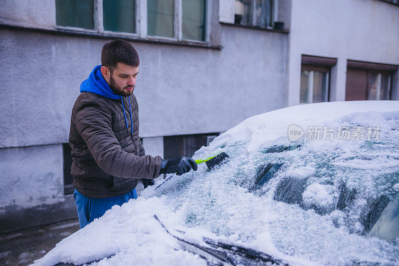 年轻人正在清除汽车上的积雪