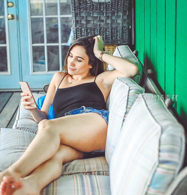 漂亮的年轻女子穿着夏装在沙发上玩手机