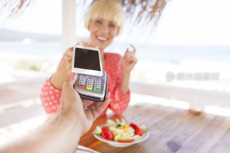 一名女子在海滩酒吧用智能手机进行非接触式支付