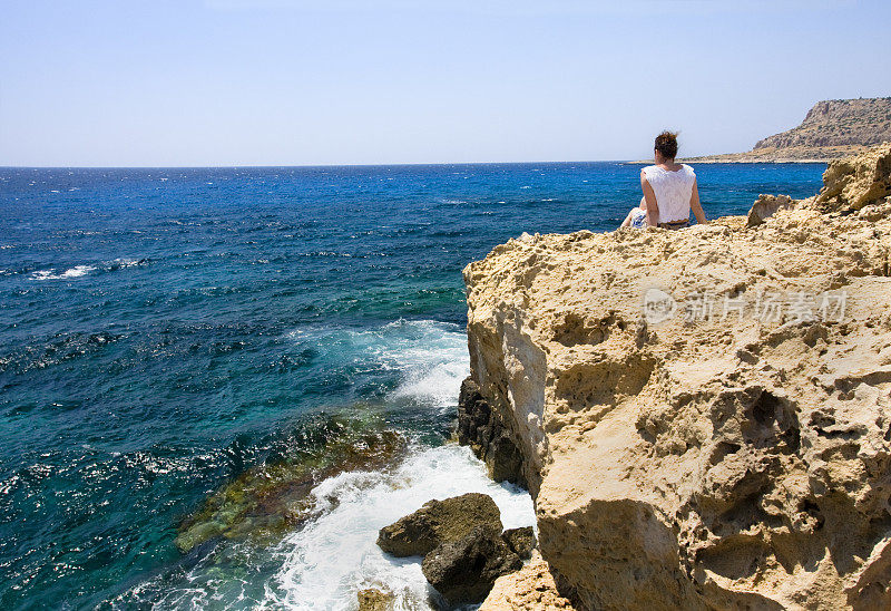 孤独的女孩坐在深海附近的岩石旁